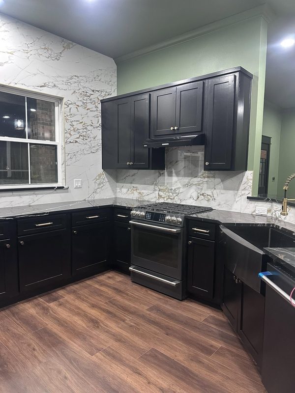 Black shaker cabinets with marble look backsplash and plank floor
