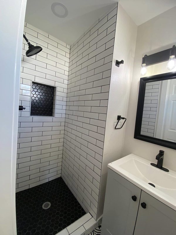 White subway tile shower with black hex floor and new vanity